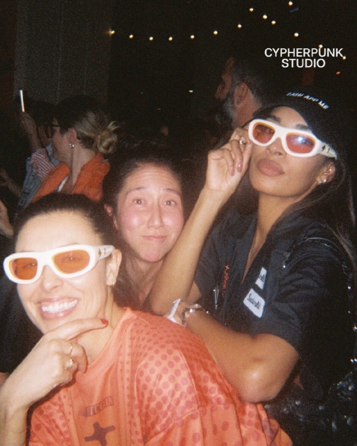 Three guests in white sunglasses under the string lights